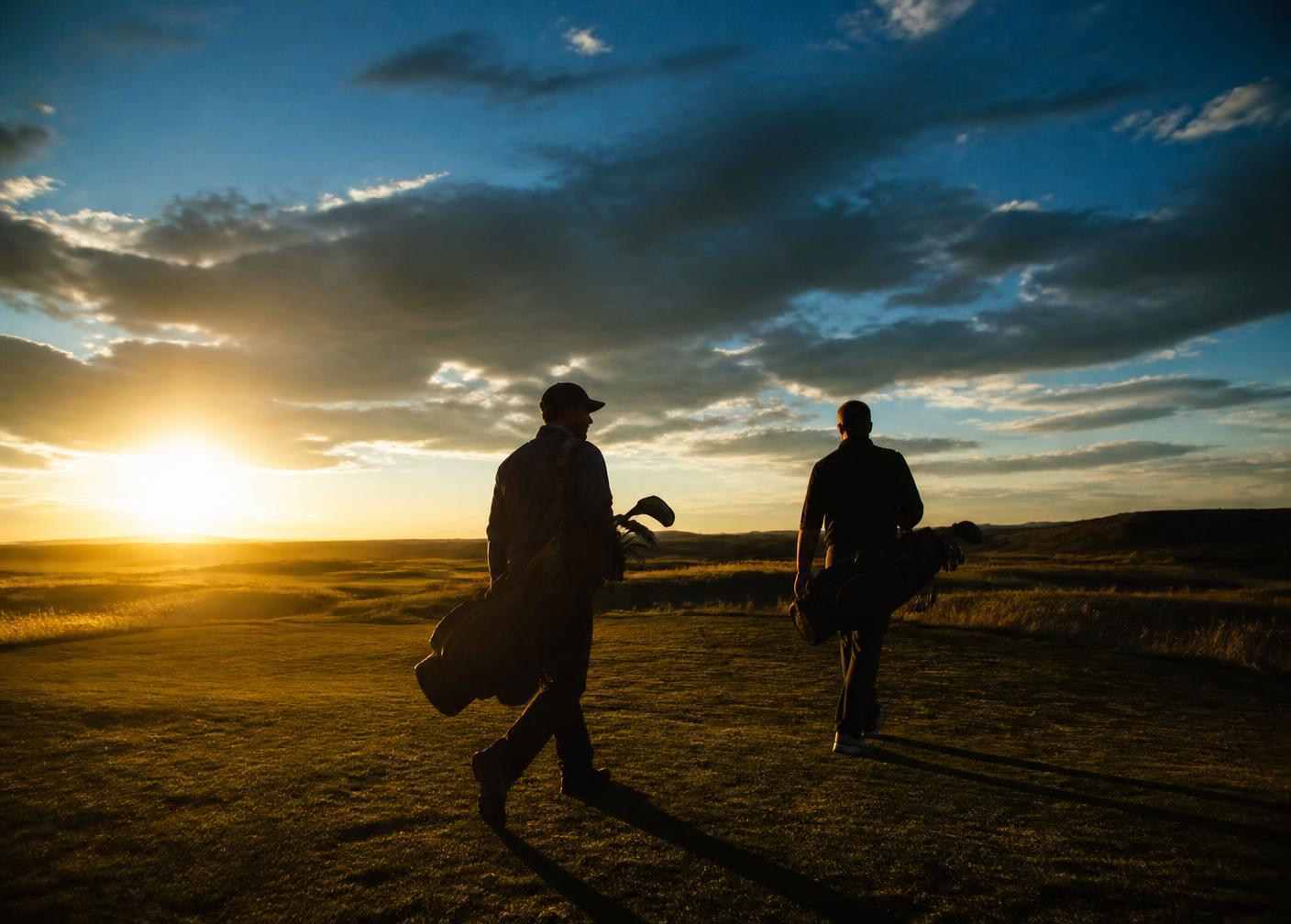 Two men walking a prairie golf course at sunset